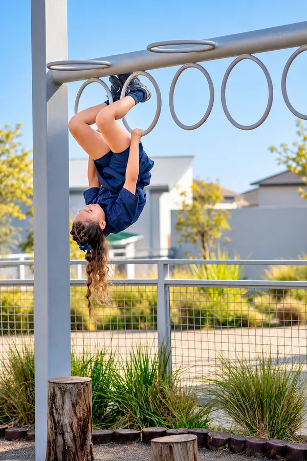 A Prep girl hanging upside down from the monkey bars, laughing