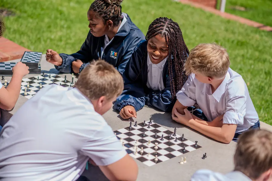 Students laughing together over a game of outdoor chess in the sun