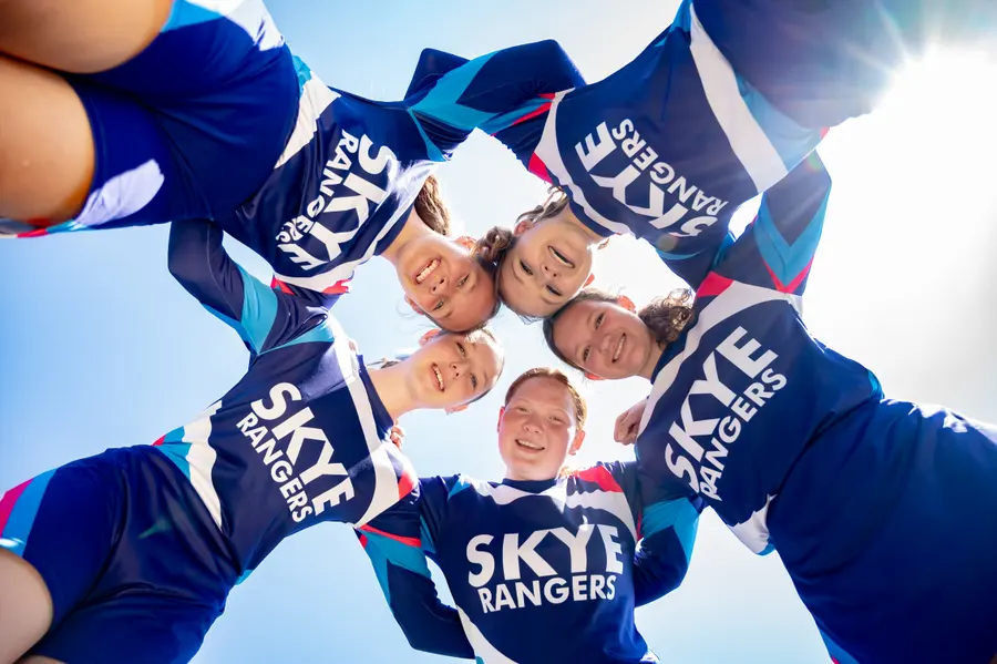 Skye Rangers cheerleaders in a huddle, seen from below against a blue sky